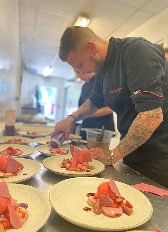 A tattooed chef plating lobster dishes in the professional kitchen of Bistrot du Lac in Bordeaux