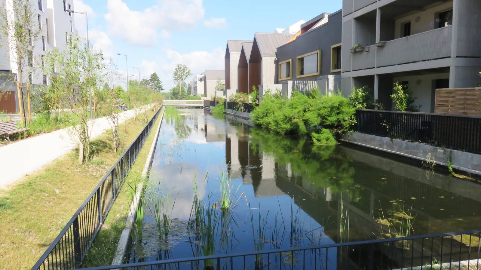 Canal view with modern buildings and contemporary architecture at Bordeaux Lake, surrounded by lush vegetation along the waterside