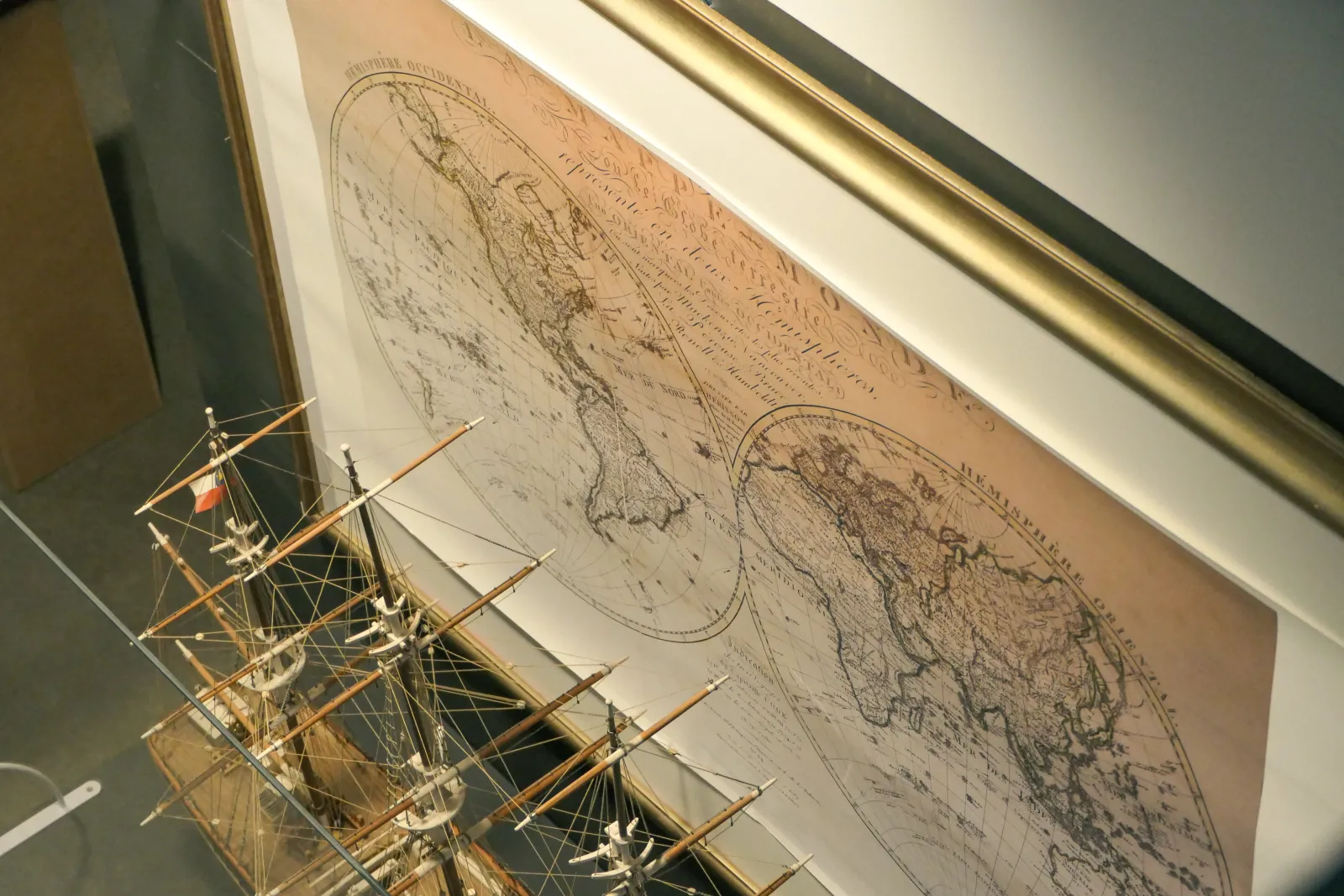 Scale model of a sailing ship displayed next to an antique maritime map at the Bordeaux Maritime History Museum