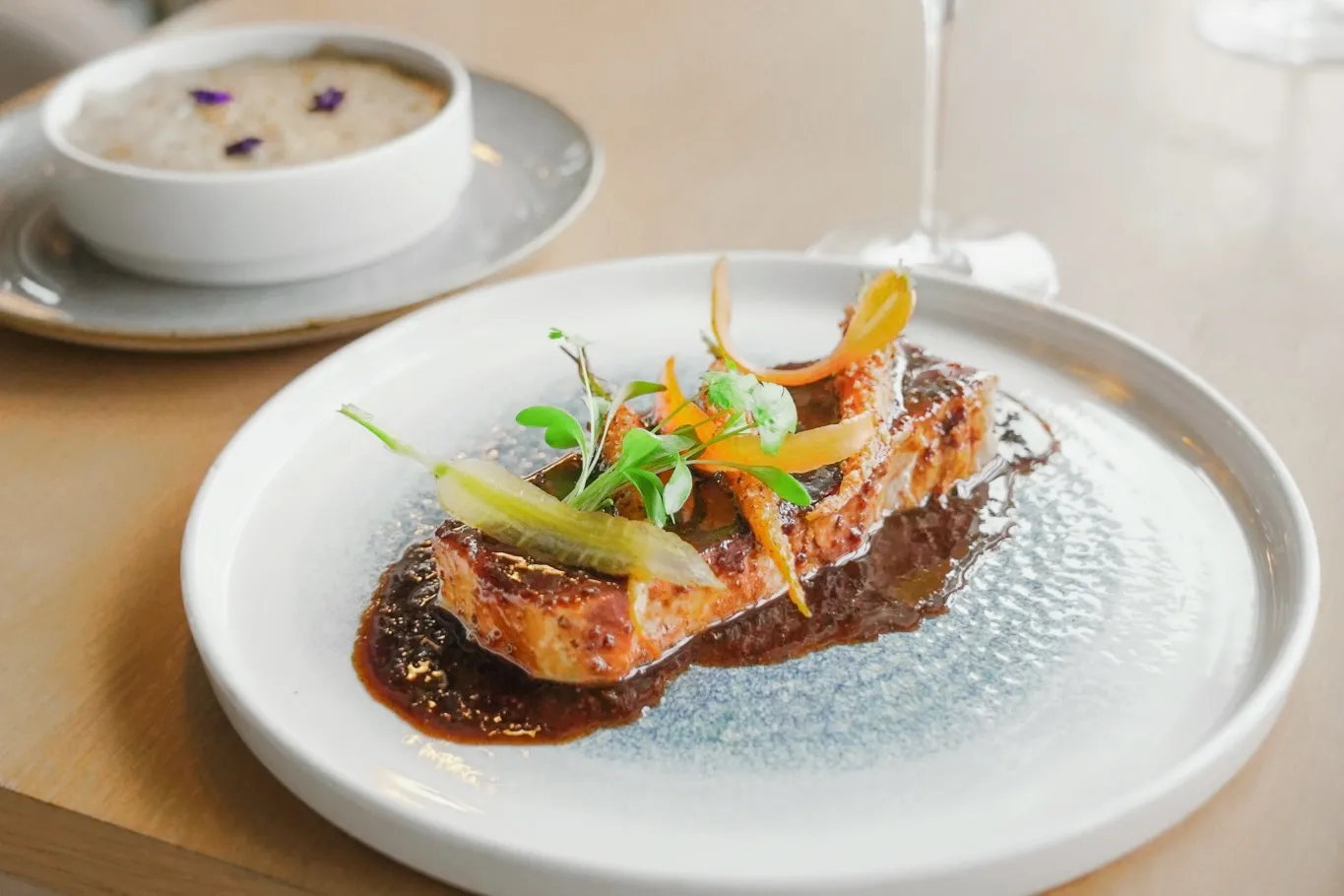 Fine dining plate featuring seared foie gras with dried fruits and colorful garnishes, accompanied by a soup in the background, served at Le 7 panoramic restaurant at La Cité du Vin in Bordeaux.
