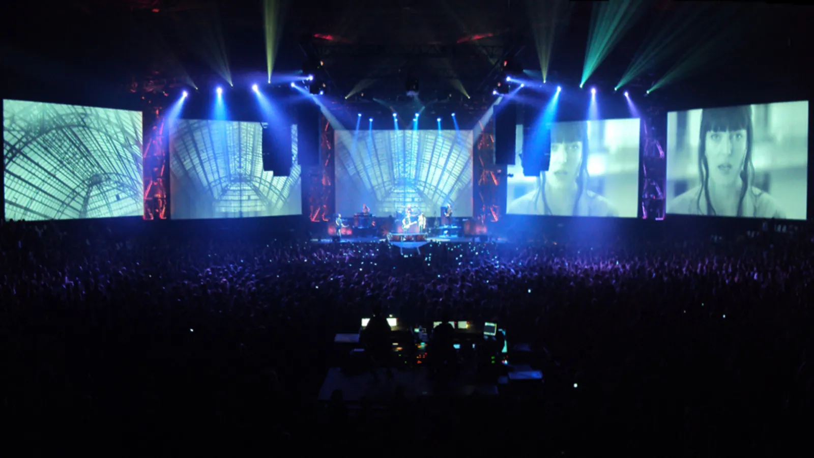 Live concert at Bordeaux's Mériadeck Ice Rink featuring a lit stage, giant screens, and audience under blue spotlights