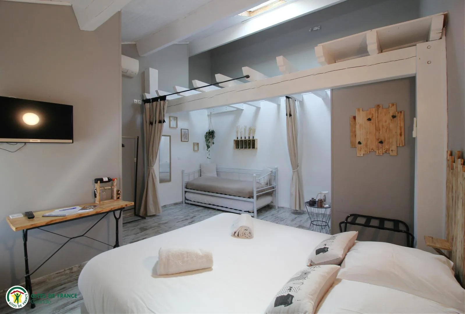 Modern guest room featuring two white beds in the foreground, a desk with TV screen, and a separate bedroom visible through a glass partition with beige curtains, decorated in minimalist contemporary style