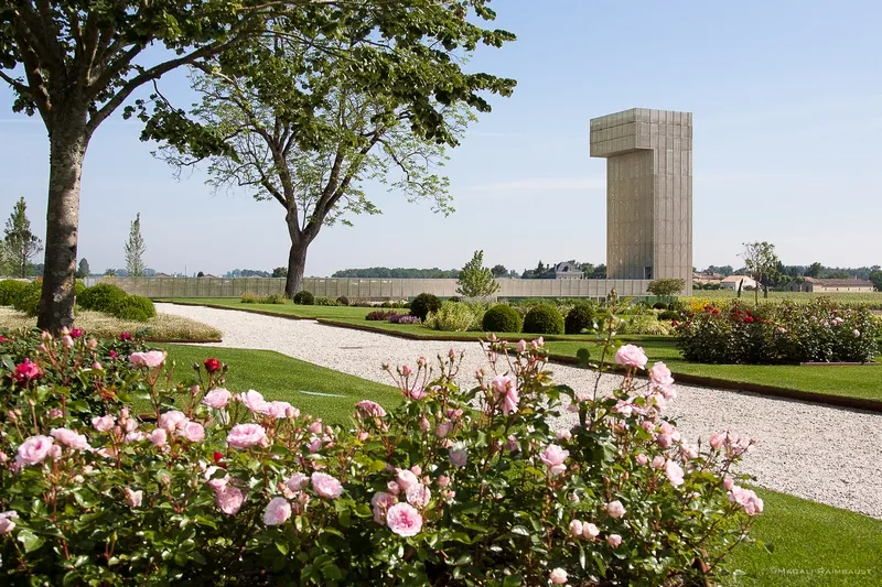 Concrete memorial tower in the gardens of Château Gruaud Larose near Bordeaux, surrounded by pink roses, trees and gravel pathways