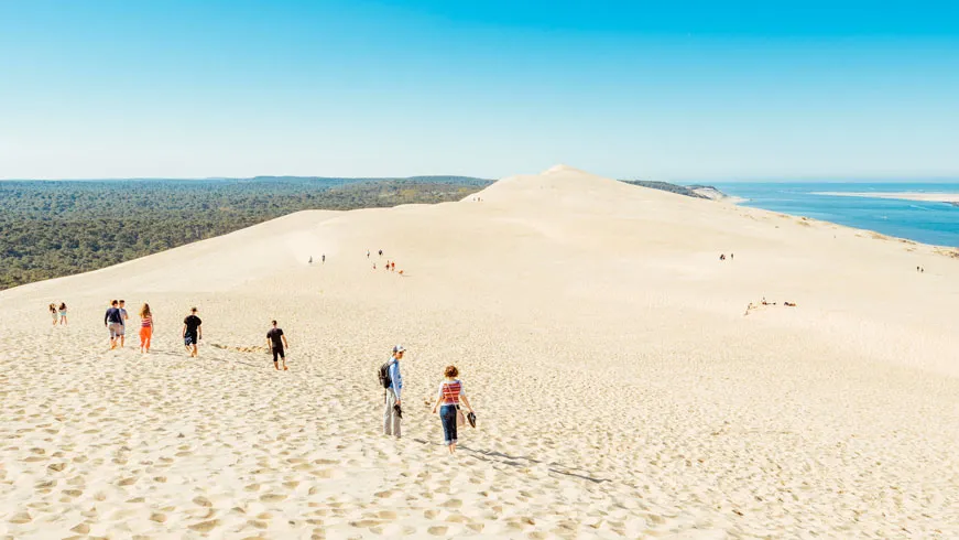 Aerial view of Dune du Pilat in Arcachon Basin with visitors on white sand, pine forest on the left and blue ocean on the right
