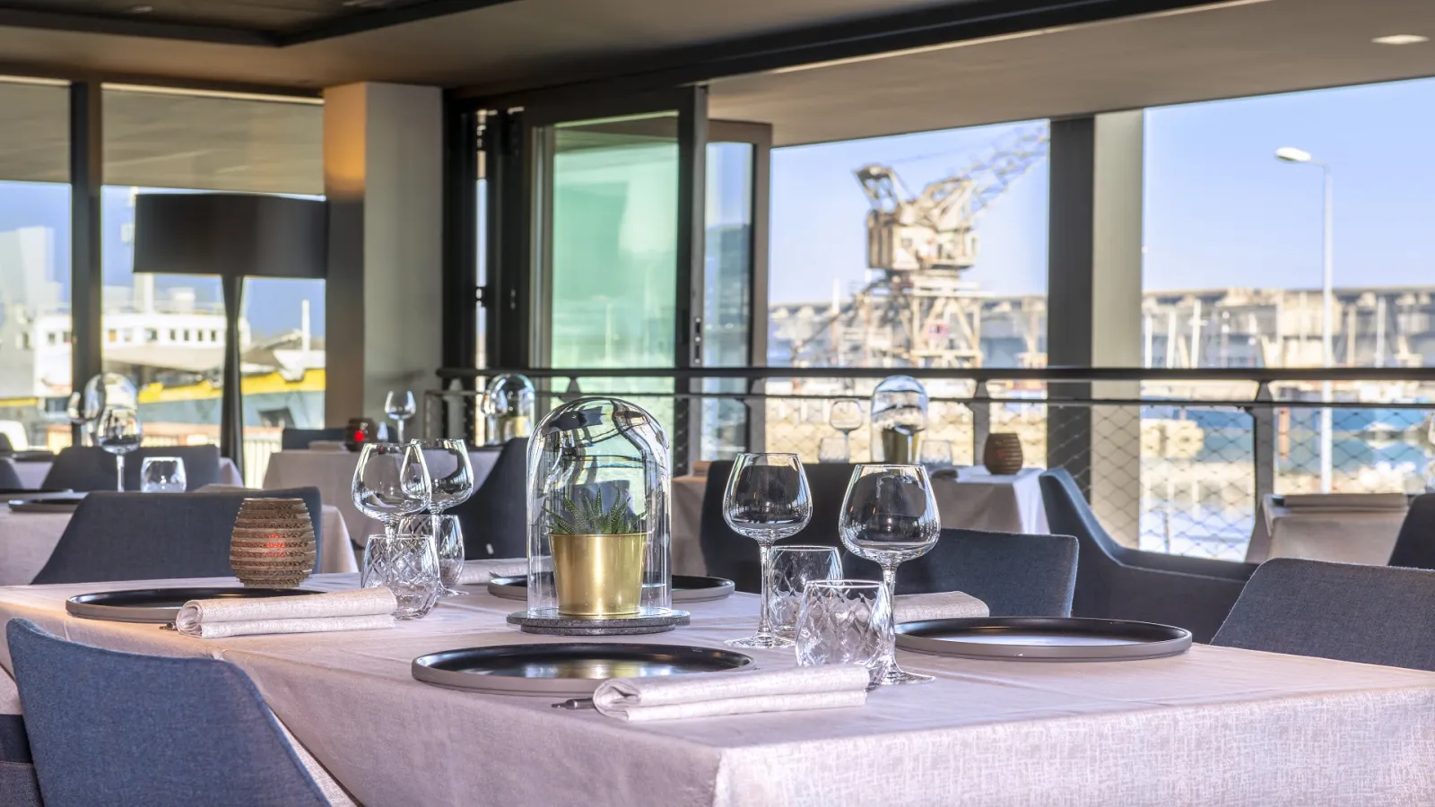 Elegant dining room at Radisson Blu Hotel Bordeaux with set tables, glassware, and cutlery, overlooking the city of Bordeaux and its riverfront.