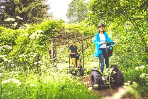 Group of people riding electric gyroscooters in a lush green garden with a plant archway and white flowers, in Bordeaux.