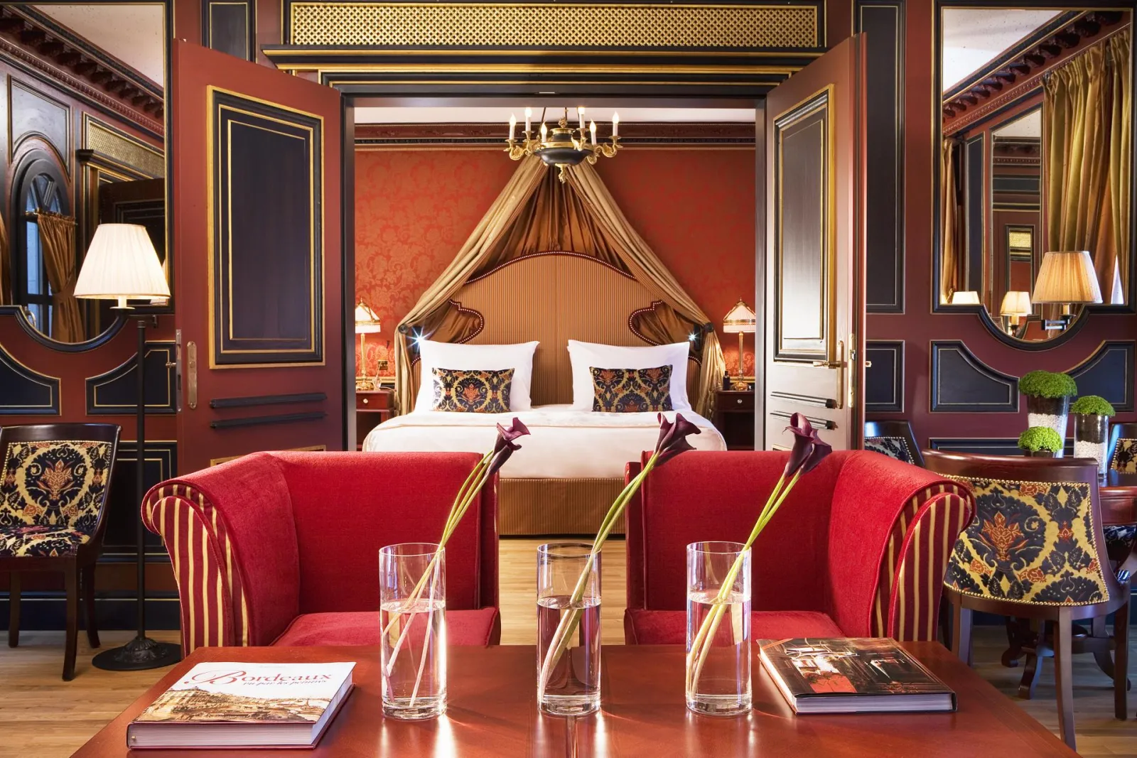 Luxury suite at Intercontinental Grand Hotel Bordeaux featuring a draped gold four-poster bed, red velvet sofas, terracotta walls and ornate baroque furnishings