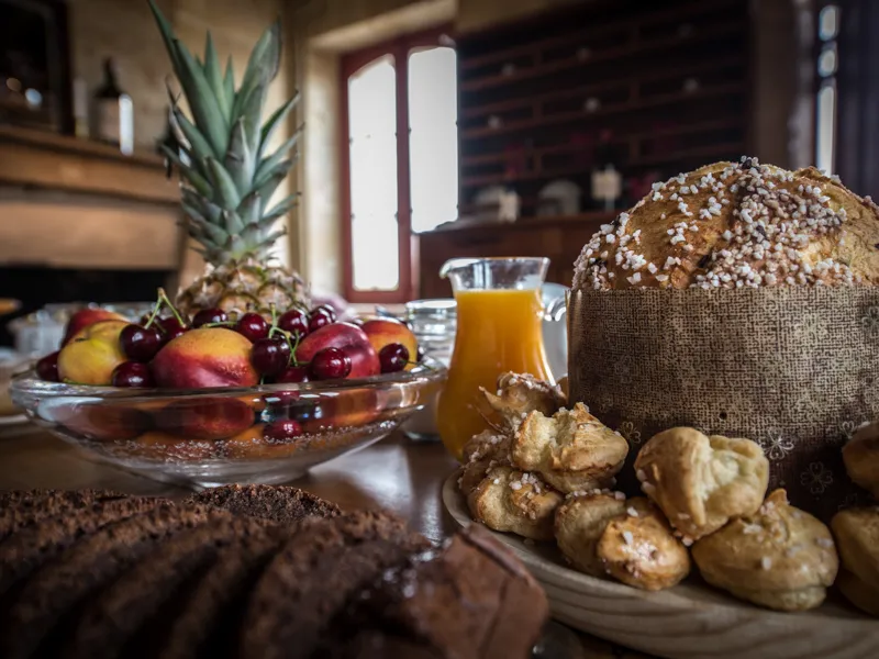 Breakfast table with fresh fruits, almond bread, orange juice and potted plant in an elegant interior with glass doors