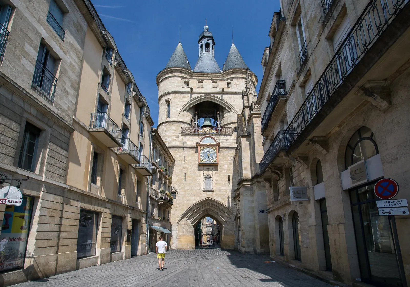The Grosse Cloche of Bordeaux, a 13th-century medieval tower with three conical turrets, framed by historic buildings on a paved street in the old town.