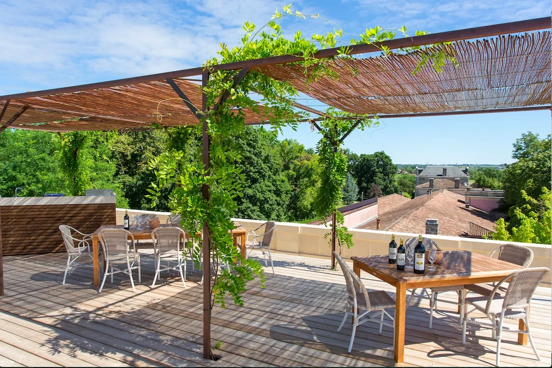Shaded terrace at Château Siran in Bordeaux featuring a wooden pergola, garden furniture, and wine tasting tables overlooking the vineyards and Bordeaux region.