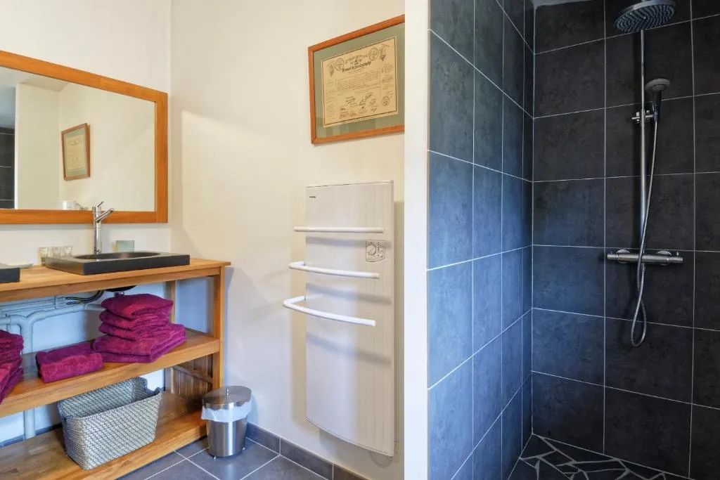 Modern bathroom featuring a black basin on wooden vanity, framed mirror, magenta towels, white radiator, and walk-in shower with black and blue tiling