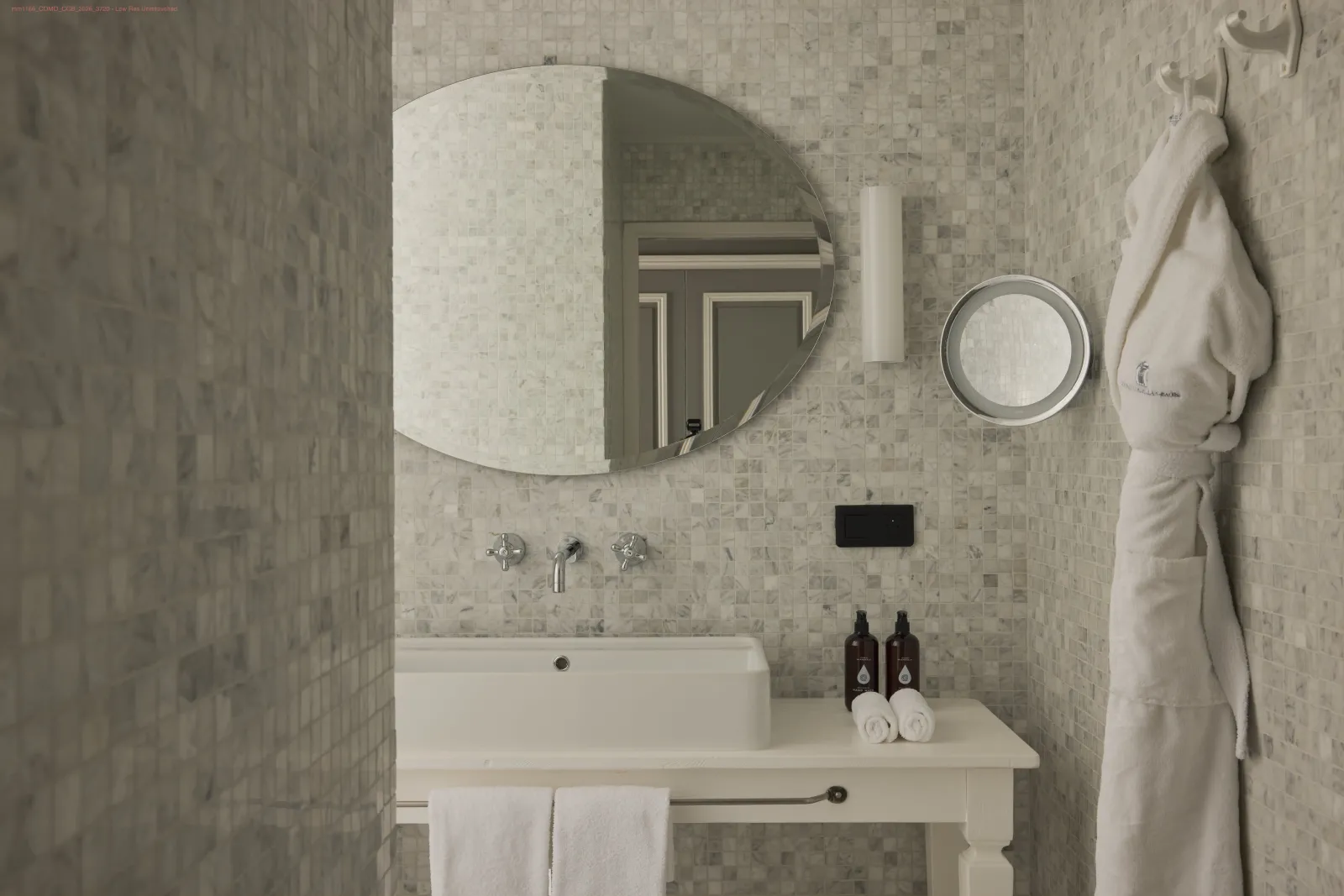 Elegant bathroom with rectangular white sink, round and oval mirrors, light beige tile walls, white towels and luxury products on the counter