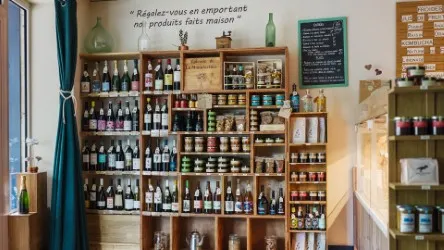 Wooden shelves stocked with wine bottles, local products and handmade items at La Manufacture Le Bayon in Bordeaux, featuring a French welcome sign and wall poster.