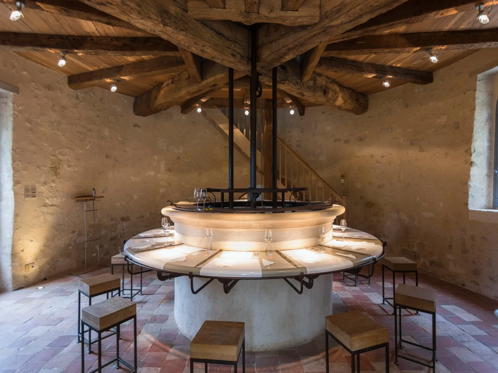 Interior of a chapel at Château de Reignac in Bordeaux featuring a modern circular altar, exposed wooden beams, raw stone walls, and wooden chairs arranged in a circle.