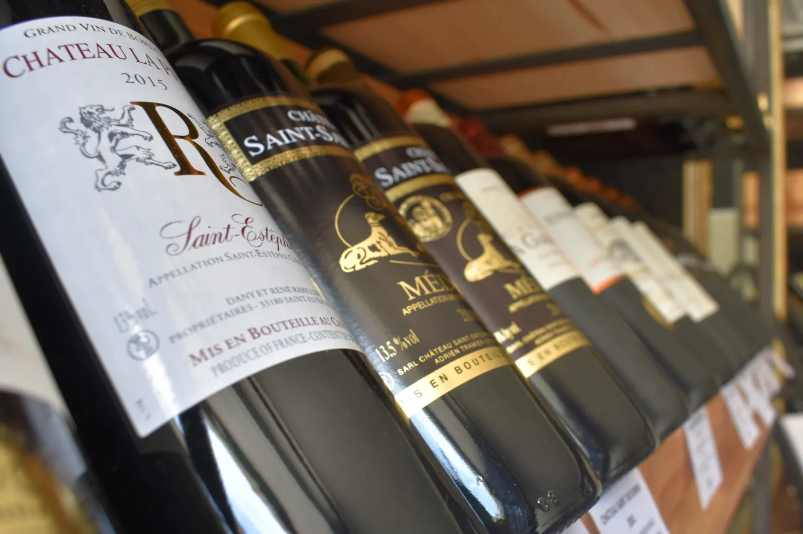 Row of Bordeaux wine bottles displayed on a shelf, featuring Château Lafite 2015 and prestigious classified growth wines with gold and black labels.