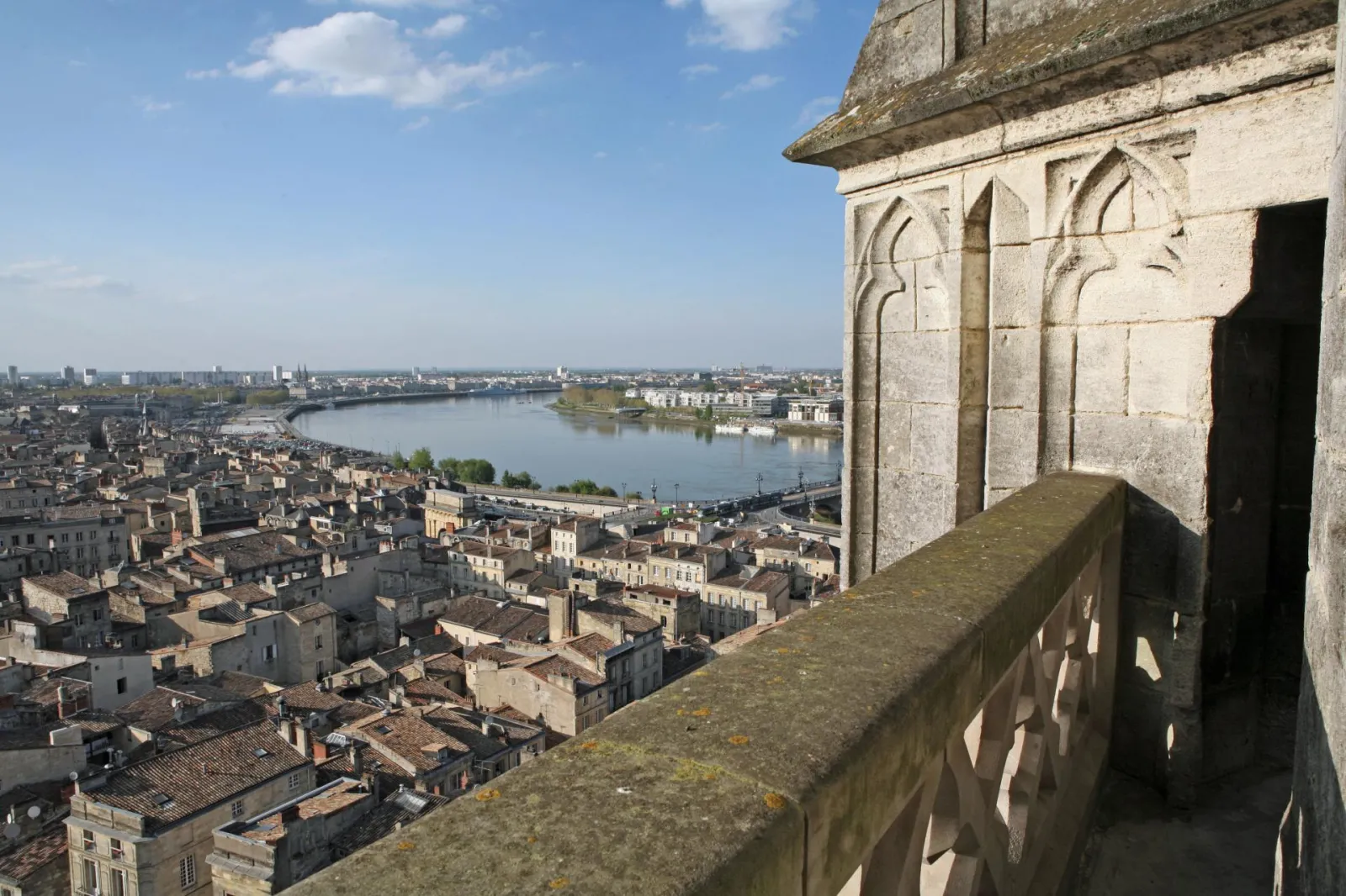 Panoramic view of Bordeaux from the Saint-Michel Spire, showing the historic city, the Garonne river, and its bridges under a blue sky.