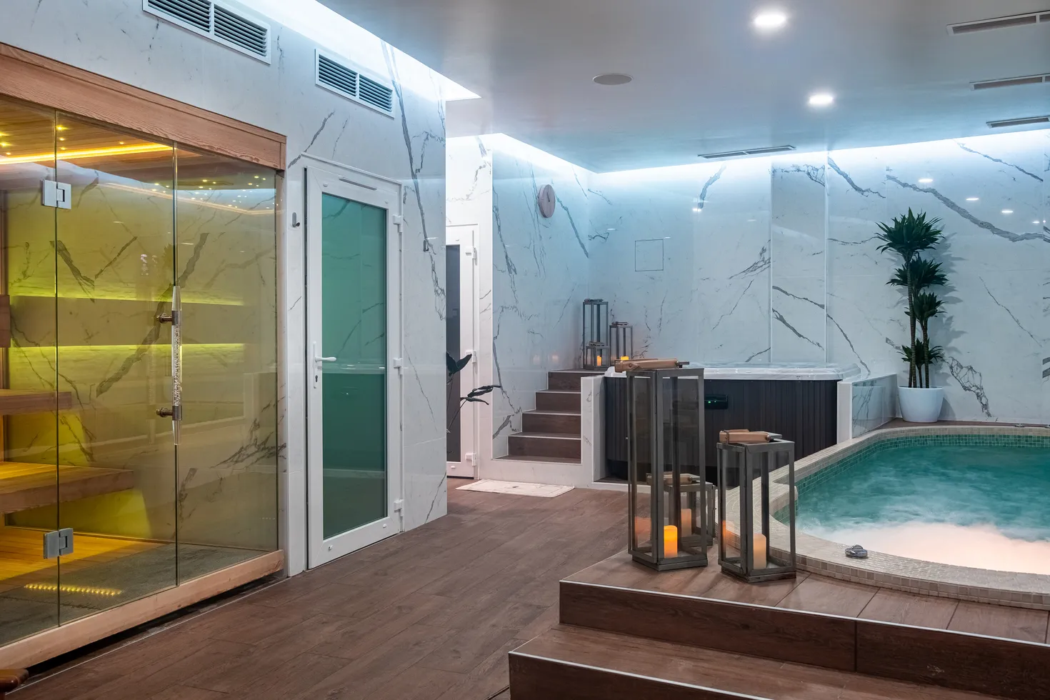 Luxurious spa facility featuring a yellow-lit sauna, turquoise pool with artificial beach, white marble walls, modern LED lighting and greenery at Spa Nuxe in Bordeaux