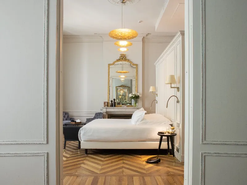 Elegant bedroom at Hôtel Villas Foch in Bordeaux featuring a white bed, herringbone parquet floor, golden mirror, gold lighting fixtures and luxury furnishings