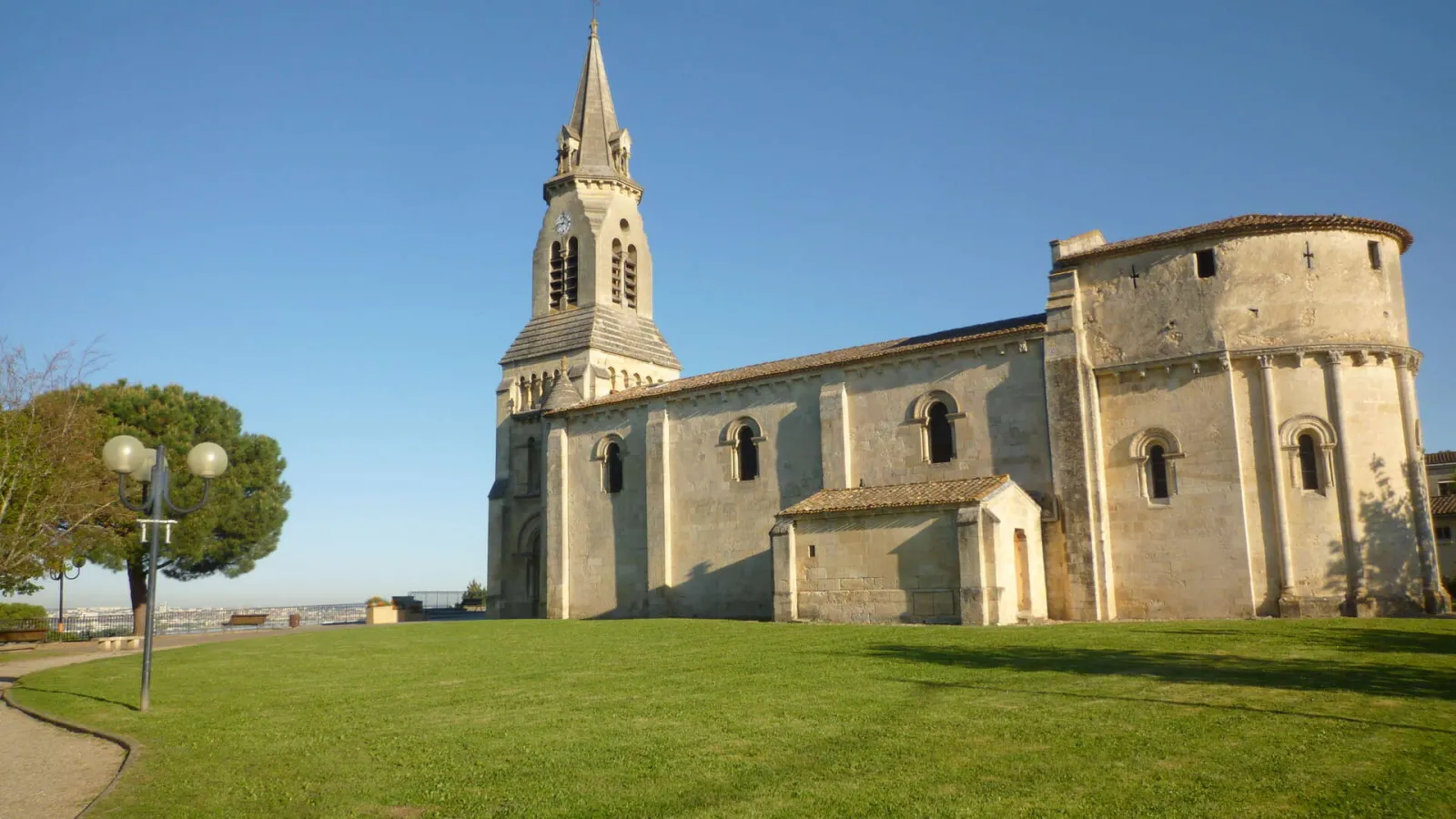 Saint-Siméon Church in Bordeaux, a stone religious building with a pointed steeple, surrounded by green lawn and parkland overlooking the city.