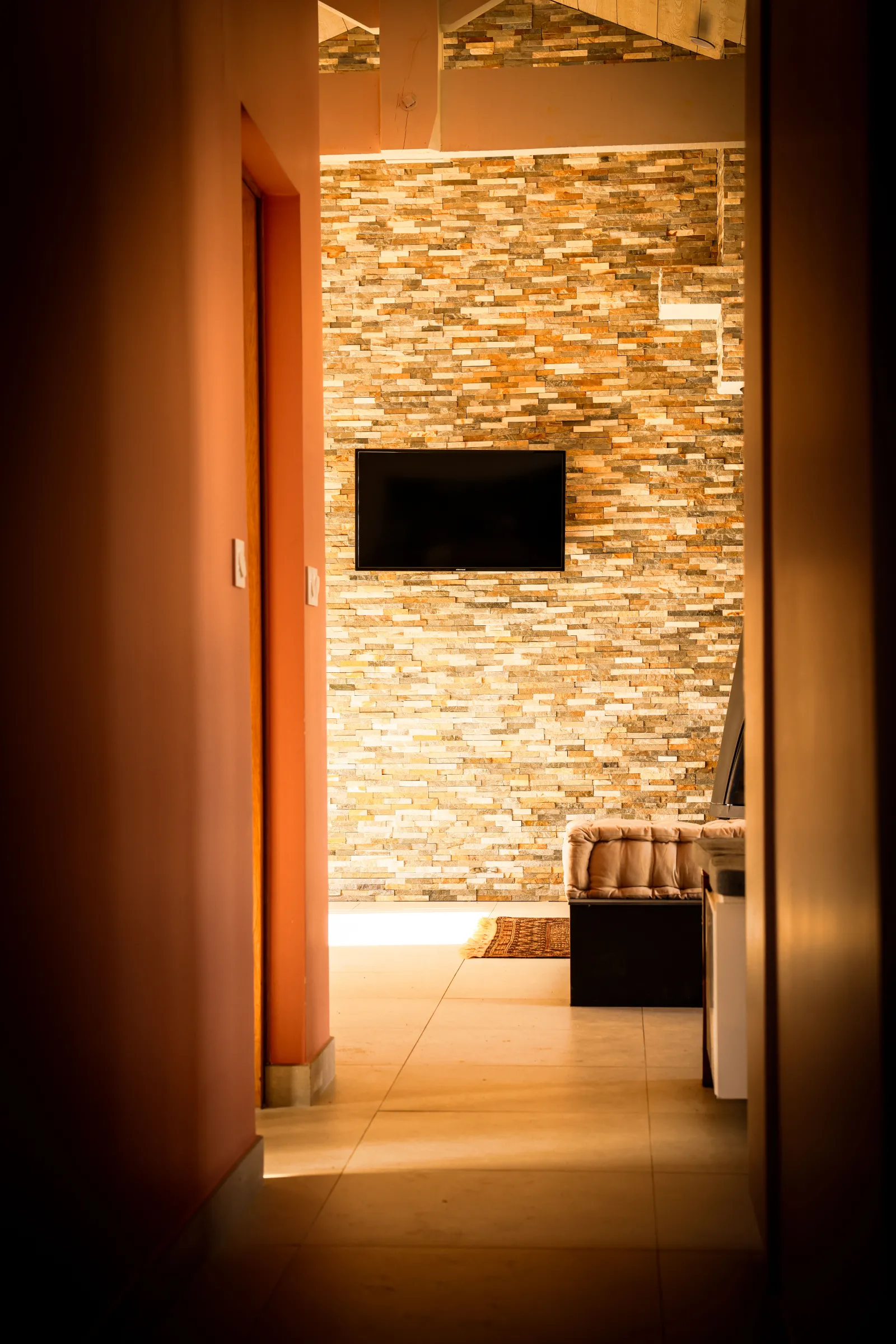Interior view of a modern hallway with orange door leading to a room with colorful brick walls, a flat-screen TV, and contemporary furniture at Eco-Cottage Alfred at Château Loudenne in Bordeaux.