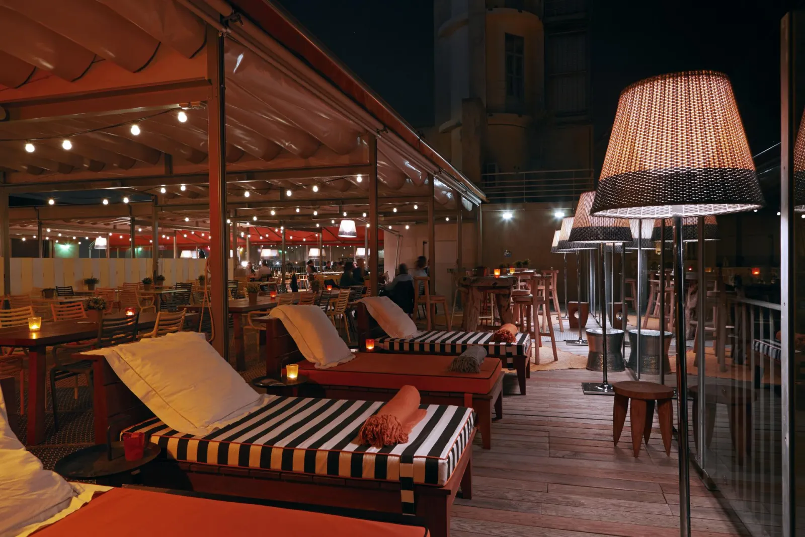 Mama Shelter Bar rooftop terrace in Bordeaux at night, featuring striped loungers, designer lamps, and warm ambient lighting
