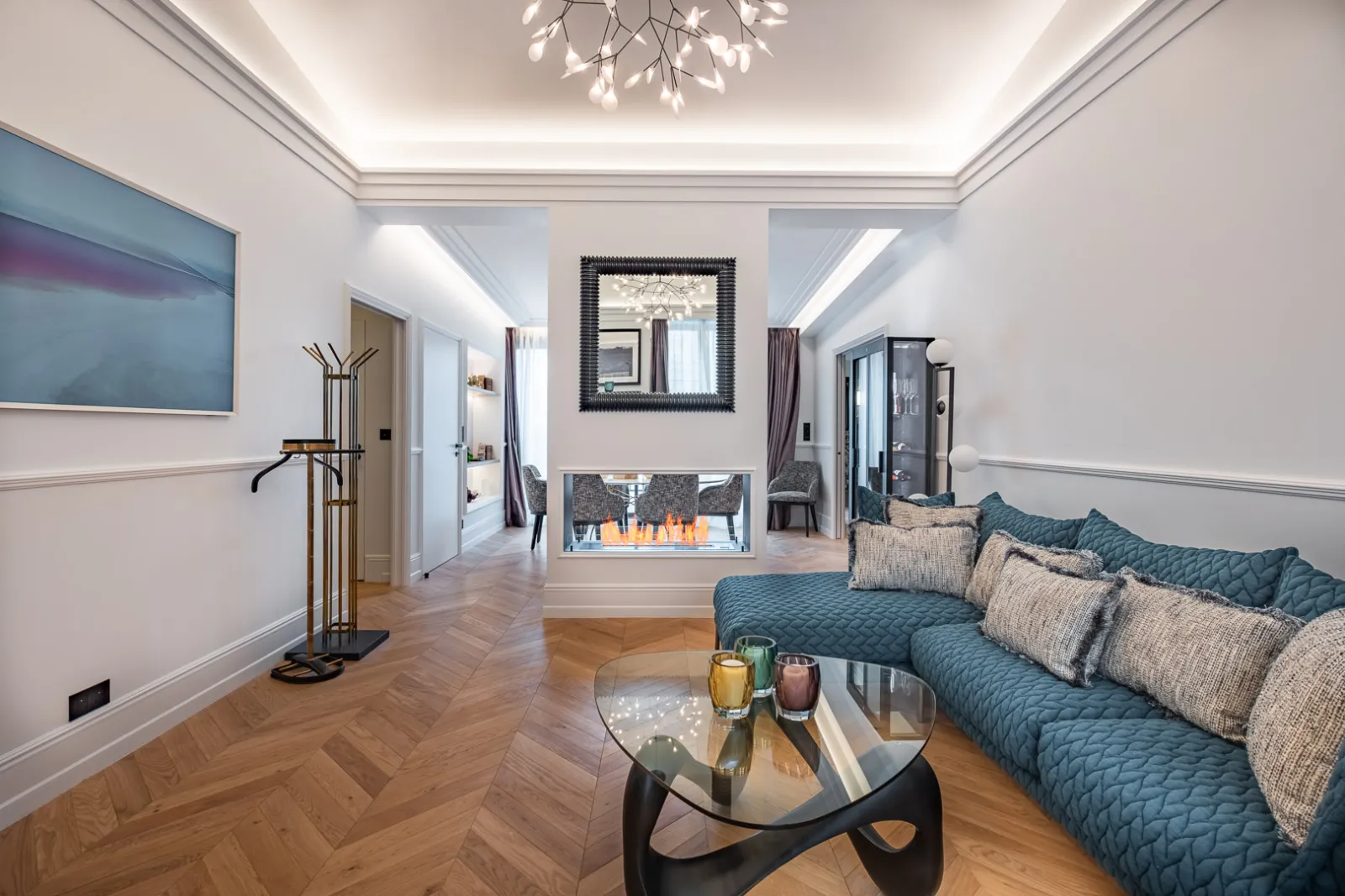 Elegant suite at Palais Gallien Hôtel & Spa in Bordeaux featuring a blue sofa, electric fireplace, framed mirror, coffered ceiling with lighting and contemporary décor