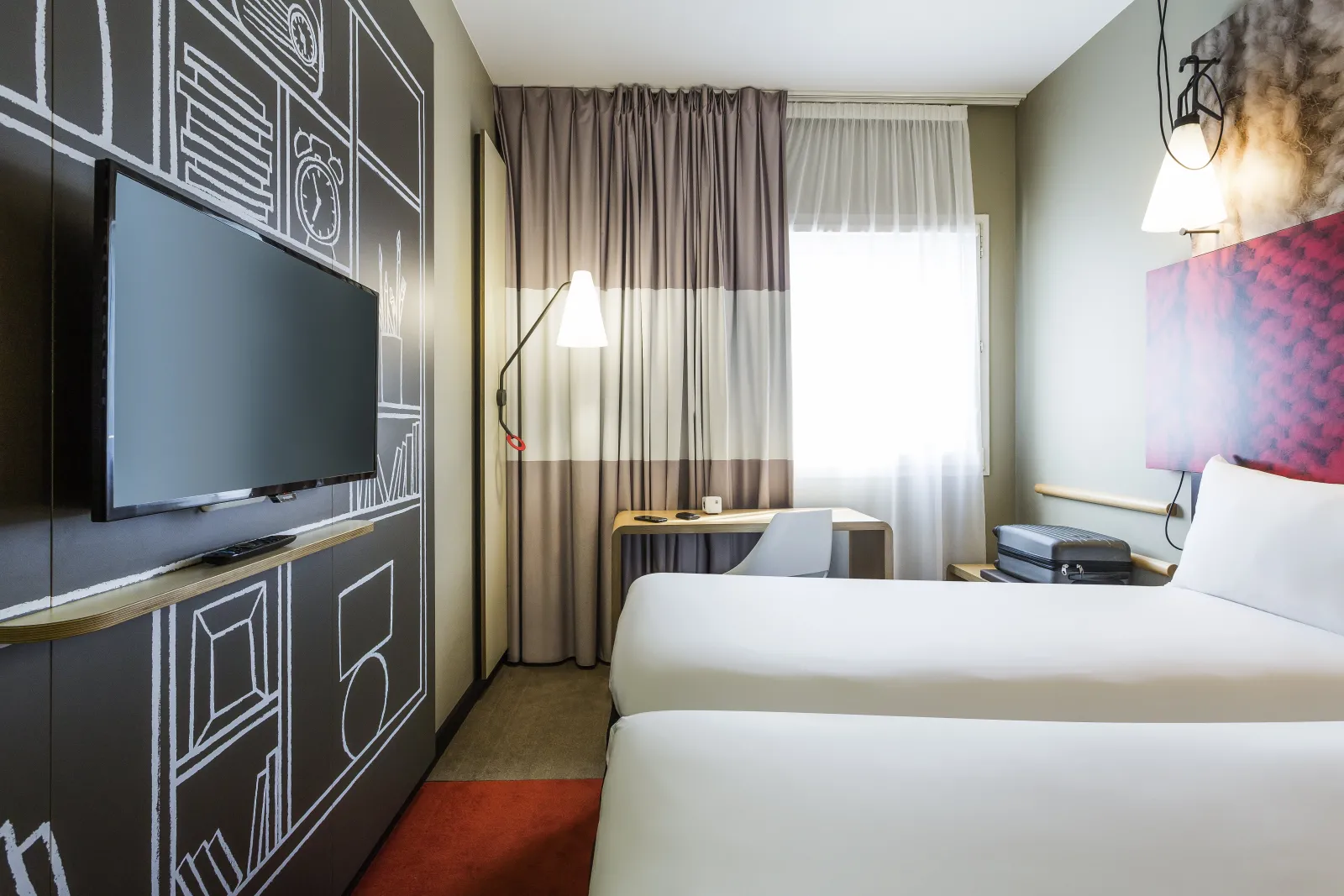 Modern hotel room with two single beds, wall-mounted TV, desk, striped curtains and contemporary decor at Ibis Bordeaux Centre Gare Saint-Jean