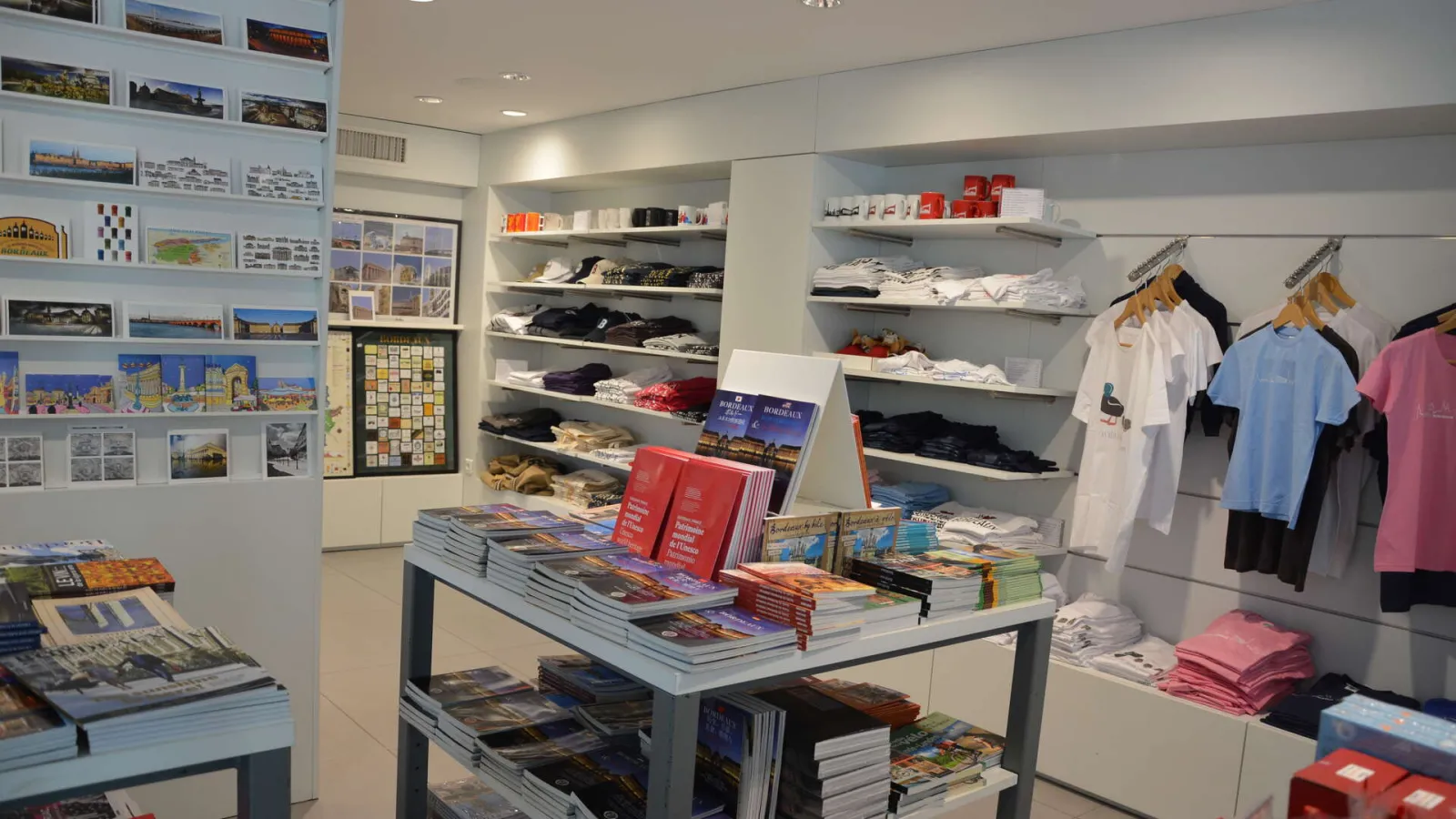 Bordeaux Tourism Office shop displaying souvenirs, travel guides, postcards, clothing and regional items on shelves and display tables.