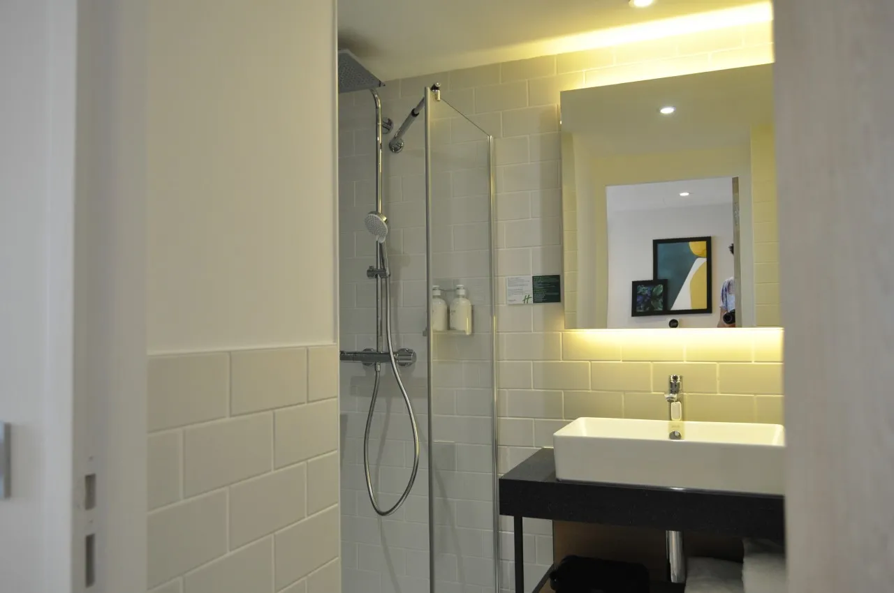 Modern bathroom with walk-in shower, white sink on black vanity, illuminated mirror and light tile at Holiday Inn Bordeaux Mérignac