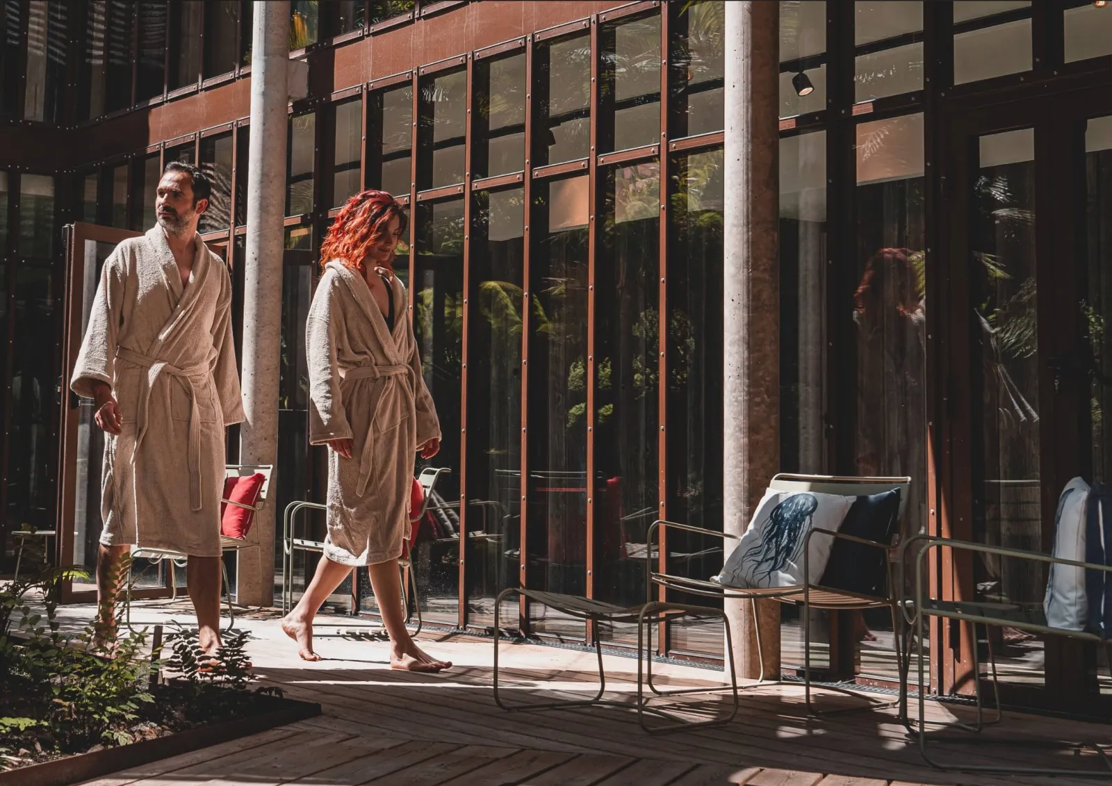 Two people in bathrobes on an indoor terrace at La Zoologie spa in Bordeaux, surrounded by plants and large glass windows.