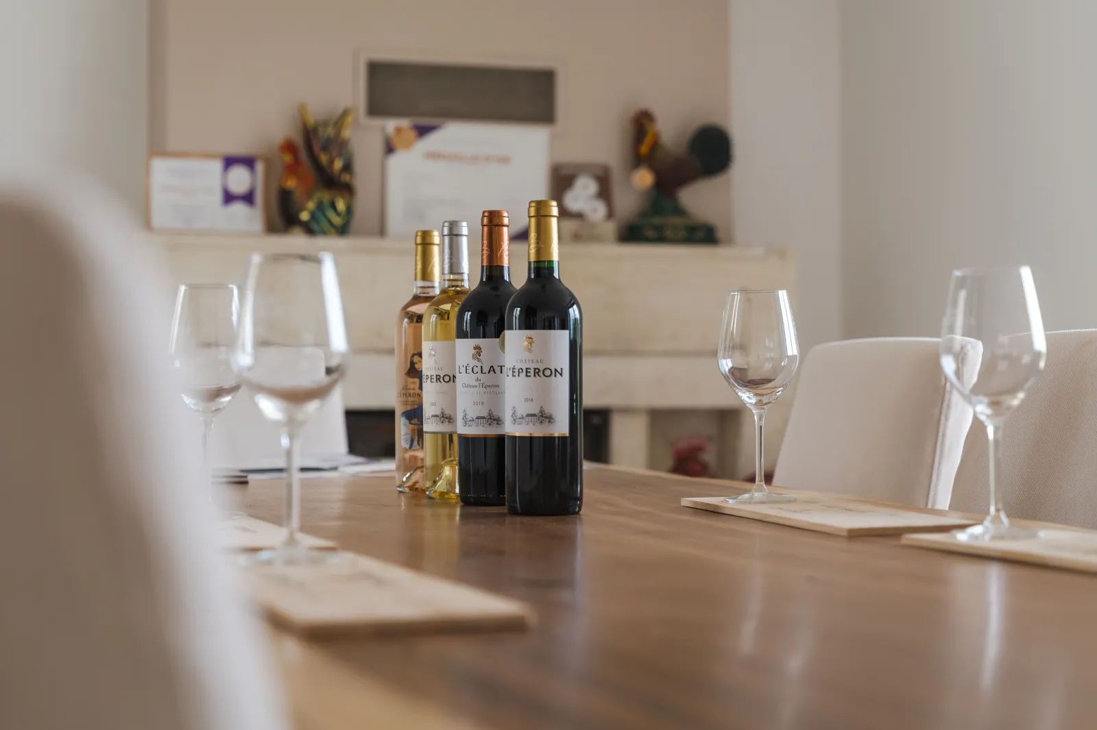 Wine tasting table at Château l'Eperon in Bordeaux featuring multiple wine bottles (rosé, white, and red) and empty wine glasses arranged on a wooden table in an elegant room with wall décor in the background.