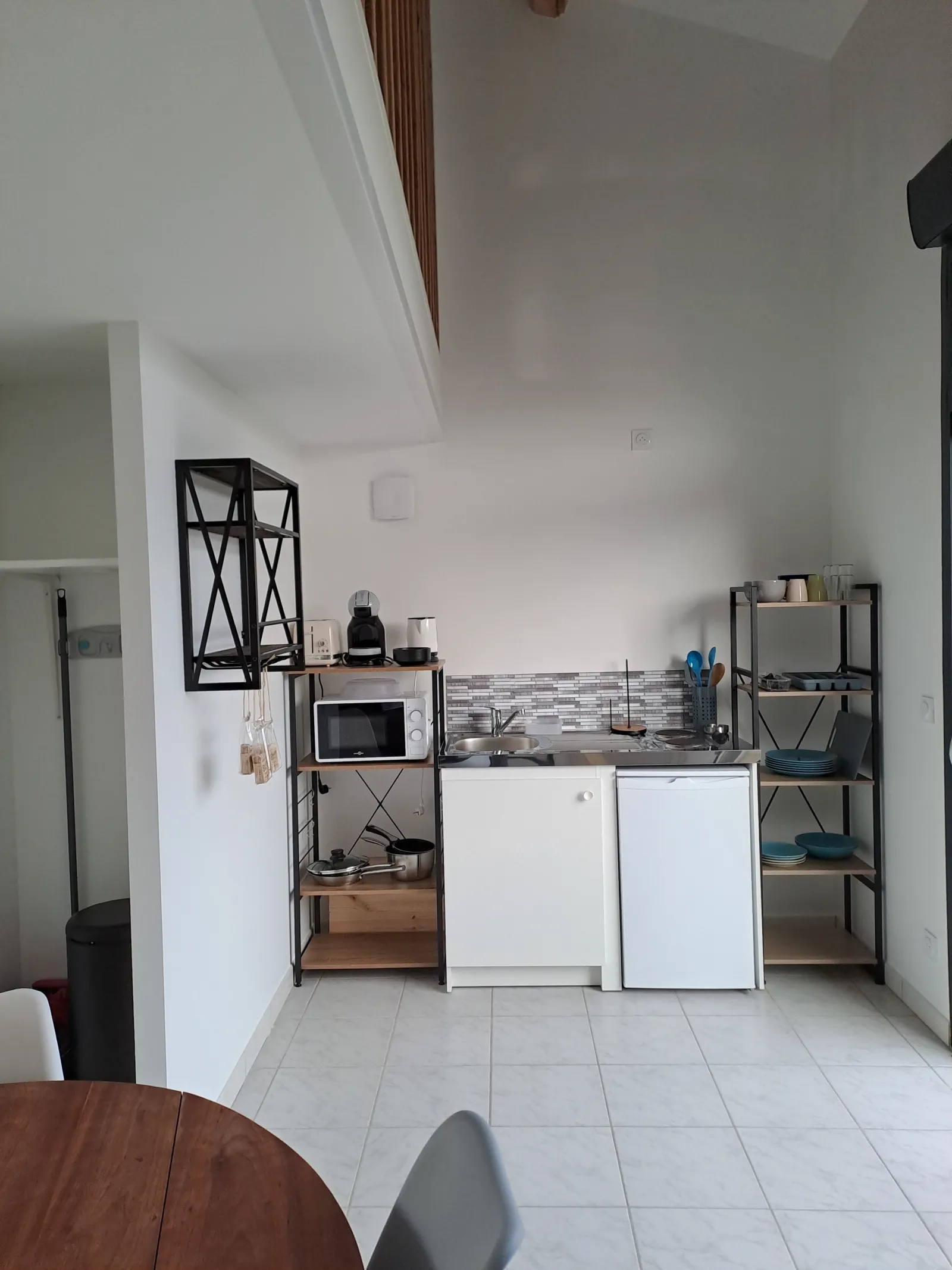 Compact equipped kitchen with white and black furniture, refrigerator, microwave and metal storage units in the Anthocyane guest house at Château Pierre de Montignac in Bordeaux