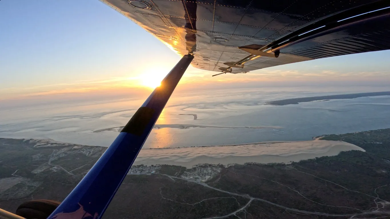 Aerial view at sunset from a small aircraft flying over Bordeaux, showing the Gironde estuary and surrounding landscape bathed in golden sunlight.