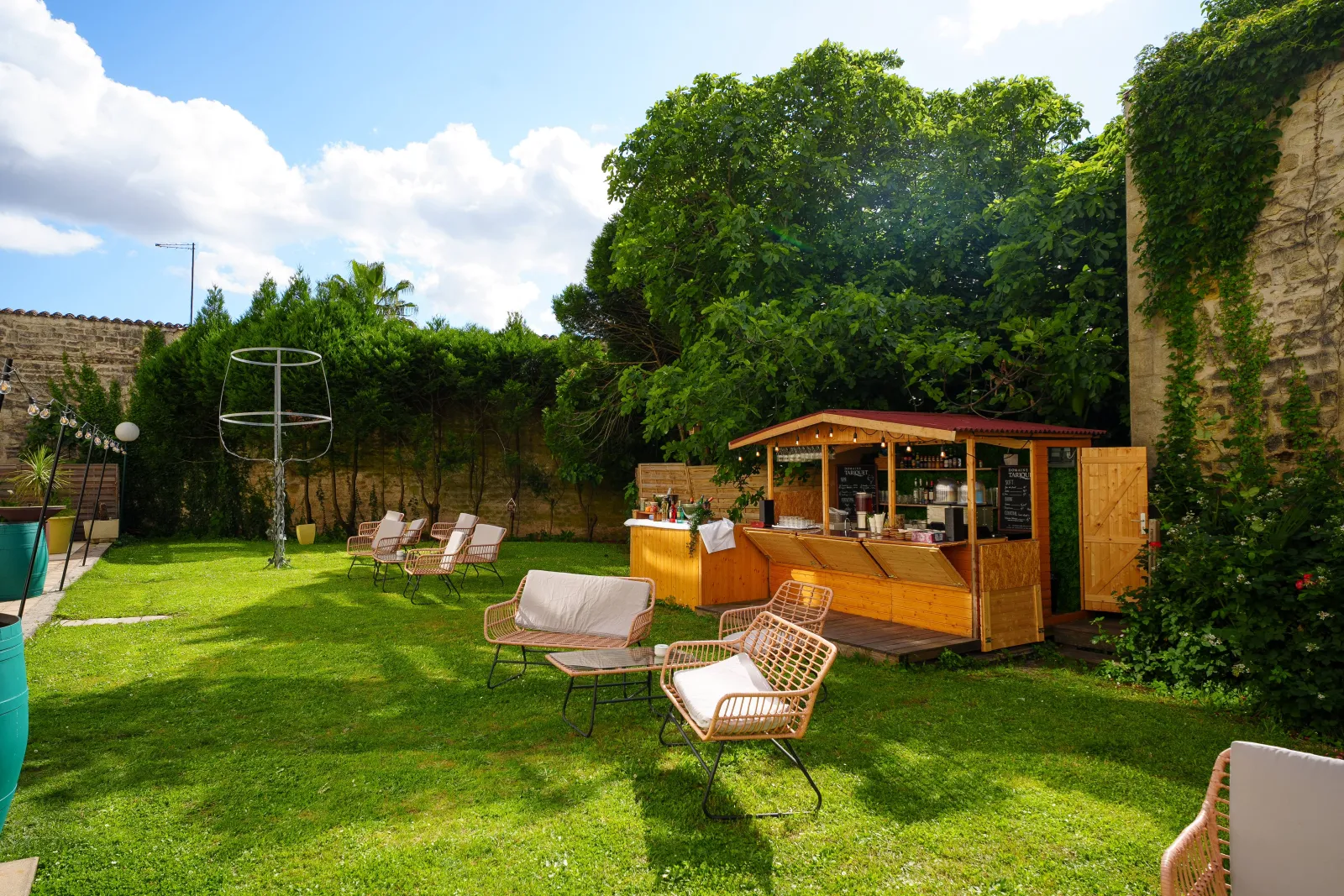 Lush garden space with wooden bar, lounge chairs and seating areas surrounded by stone walls and green vegetation in Bordeaux
