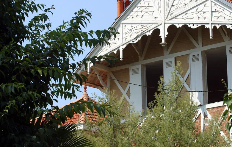 Facade of a Belle Époque villa with ornate white awning, shuttered windows, red tile roof and surrounding vegetation at Arcachon Basin.