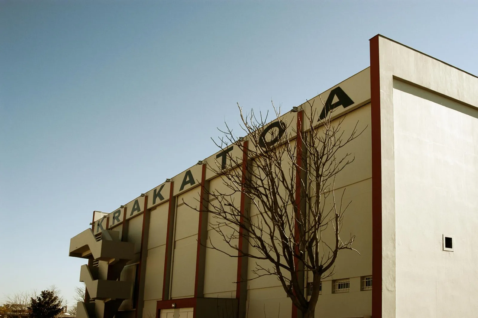 Krakatoa building facade in Mérignac, modernist architecture with white concrete structure and red beams, bare tree in foreground