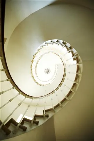 Overhead view of a white spiral staircase with geometric steps converging toward a circular light opening at the ceiling, at Château La Haye in Bordeaux.