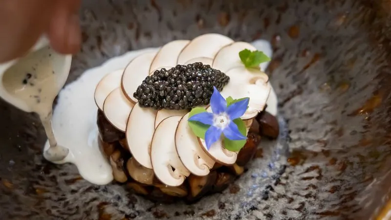 Gourmet plate from Passage Secret restaurant in Bordeaux: chocolate éclair topped with caviar, seared foie gras slices, and edible blue flower on grey sauce.