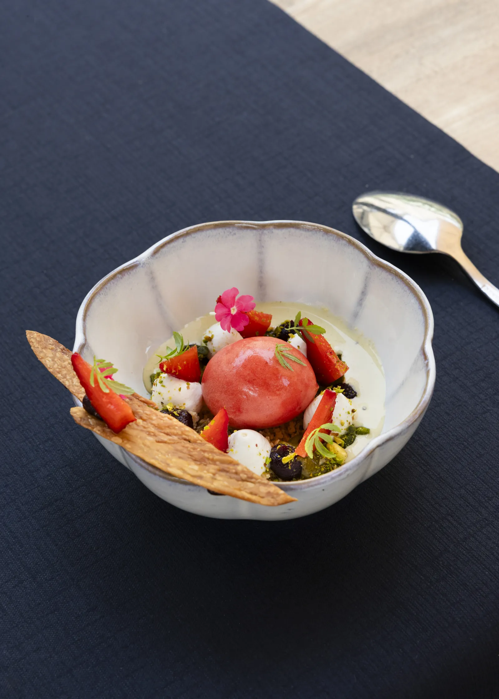 Elegant gourmet plate featuring a red tomato sphere, strawberries, white mozzarella, microgreens, a pink edible flower, and a golden tuile, presented on a dark background at Terrasse de Lafaurie in Bordeaux.