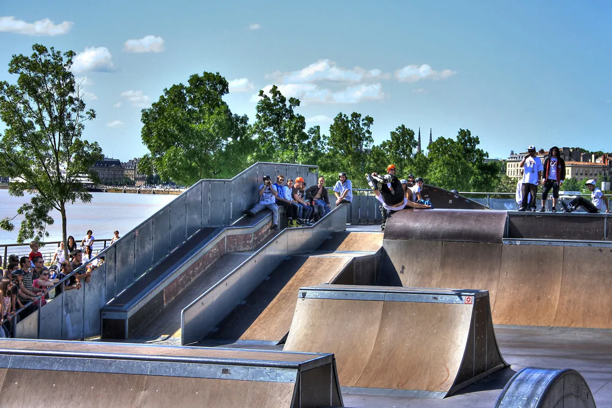 Bordeaux skate park featuring concrete ramps with skaters and spectators, overlooking the Garonne River and city architecture