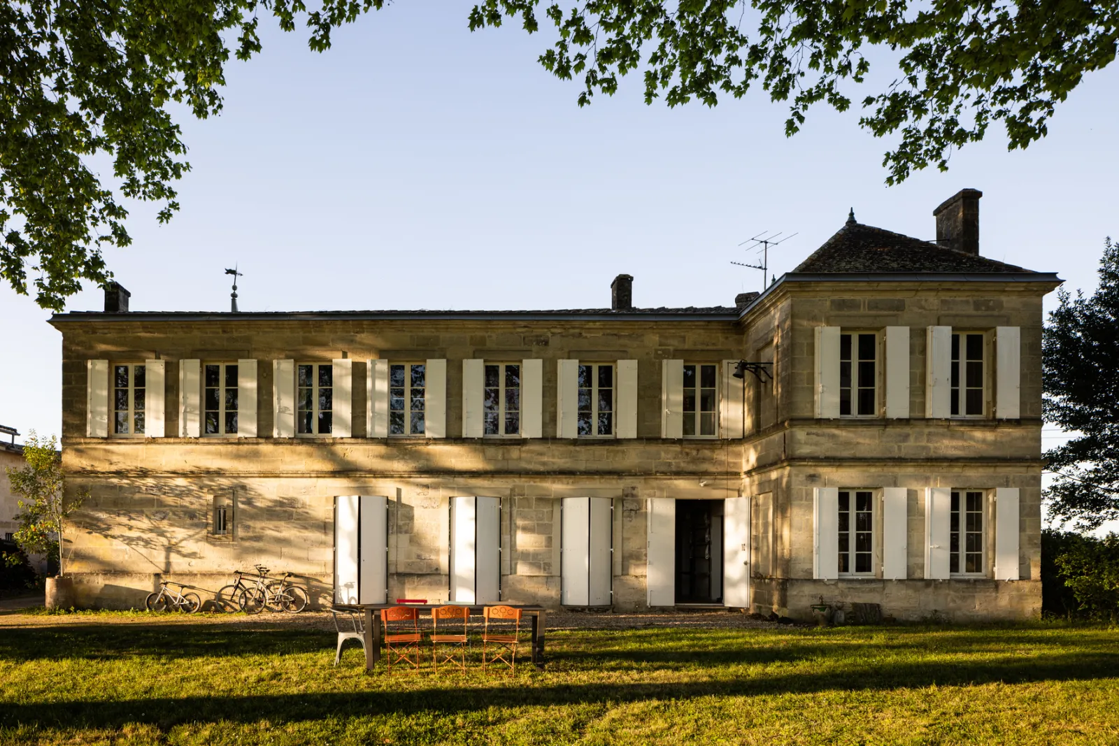 The Joualles dormitory in Bordeaux, a 19th-century ashlar stone building with white-shuttered facade, surrounded by lawn and trees, with chairs and bicycles in front of the entrance.