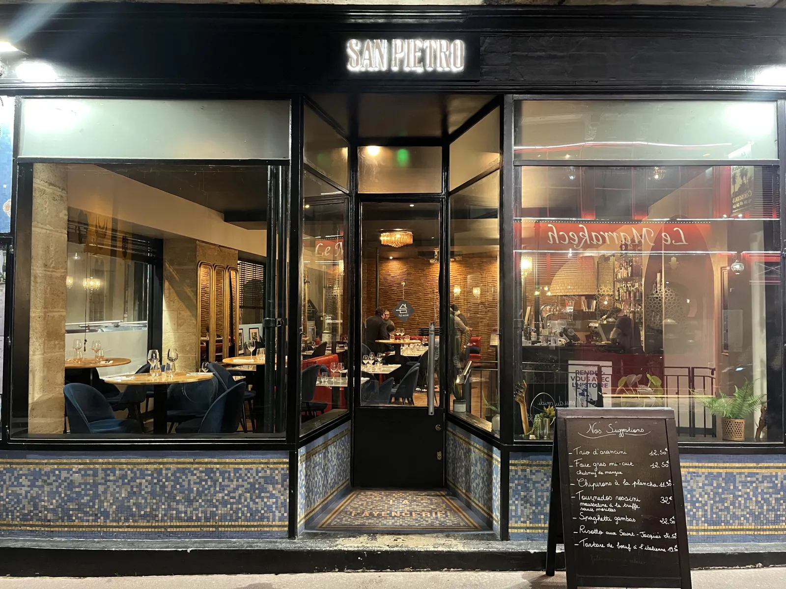 Storefront of San Pietro restaurant in Bordeaux, featuring illuminated windows displaying the interior with dining tables and guests, neon sign, and menu board at the entrance.