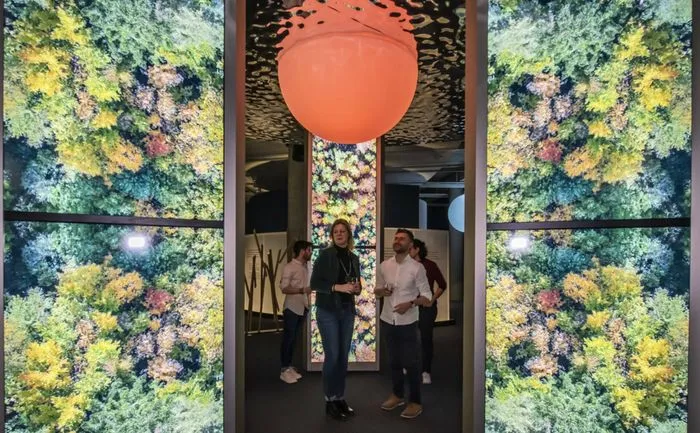 Interior of La Cité du Vin in Bordeaux displaying the Via Sensoria sensory journey with visitors walking past lush green walls and a suspended orange sphere.