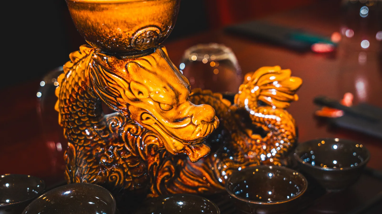 Ornate shot glasses with golden dragon motifs filled with amber liqueur, decorated with sparkling beads on a dark surface