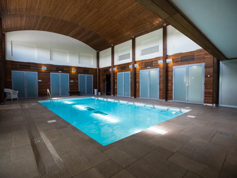 Indoor heated thermal swimming pool at Les Bains de Margaux spa in Bordeaux, surrounded by wooden changing rooms with arched wooden ceiling and natural lighting