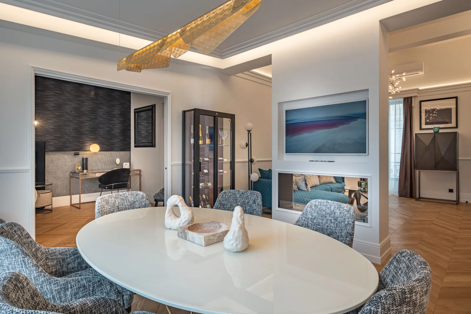Luxury suite at Palais Gallien Hôtel & Spa in Bordeaux featuring a white round table, blue chairs, bedroom with bed and wall-mounted screen, desk, golden chandelier and contemporary décor