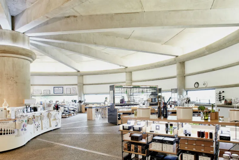 Modern interior of a cosmetics shop at Château Prieuré-Lichine in Bordeaux, featuring exposed concrete ceiling, light wood counters, and shelving displaying beauty products.
