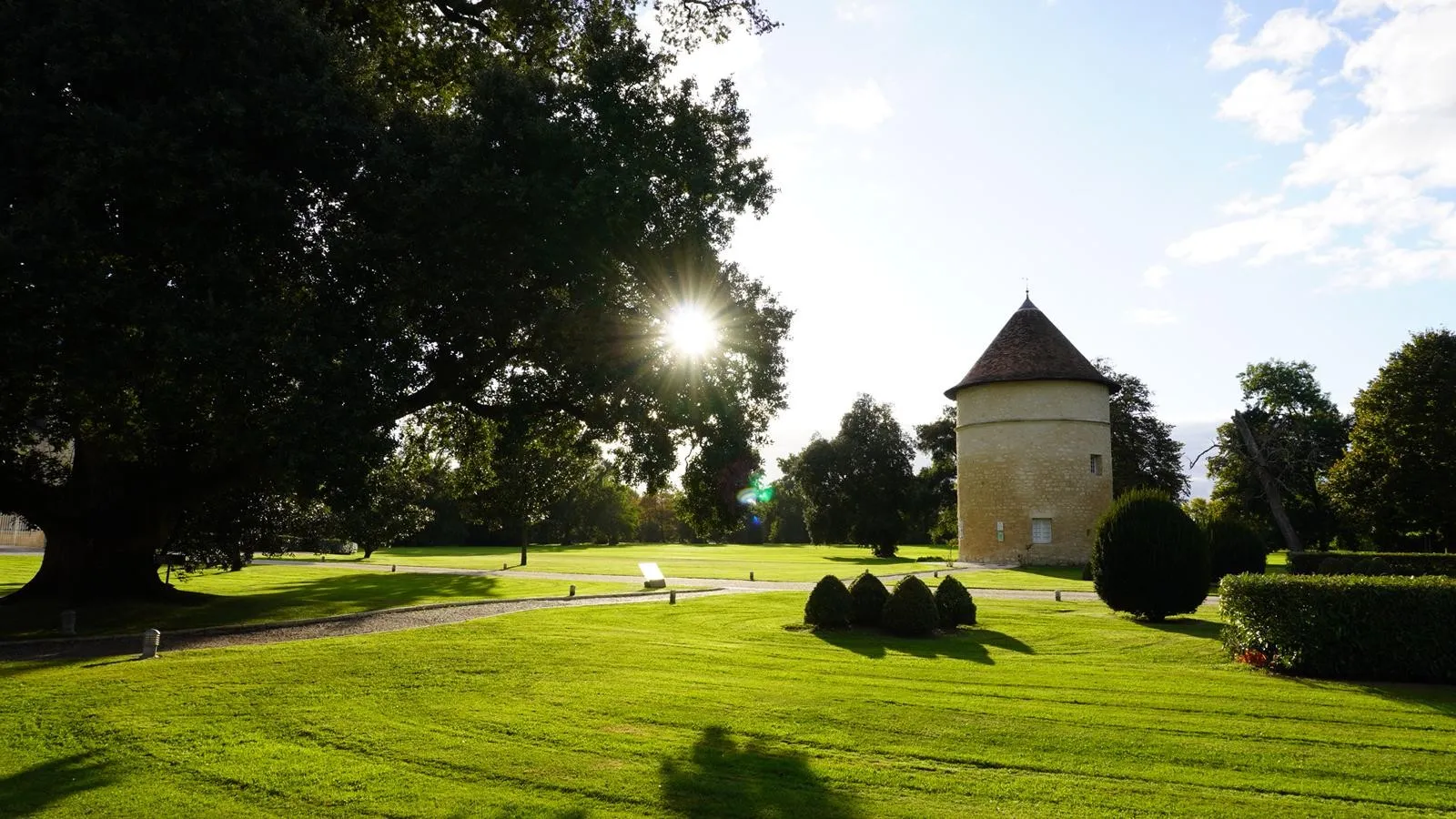 Château d'Agassac near Bordeaux featuring its distinctive round tower with conical roof, set in expansive green grounds surrounded by mature trees.