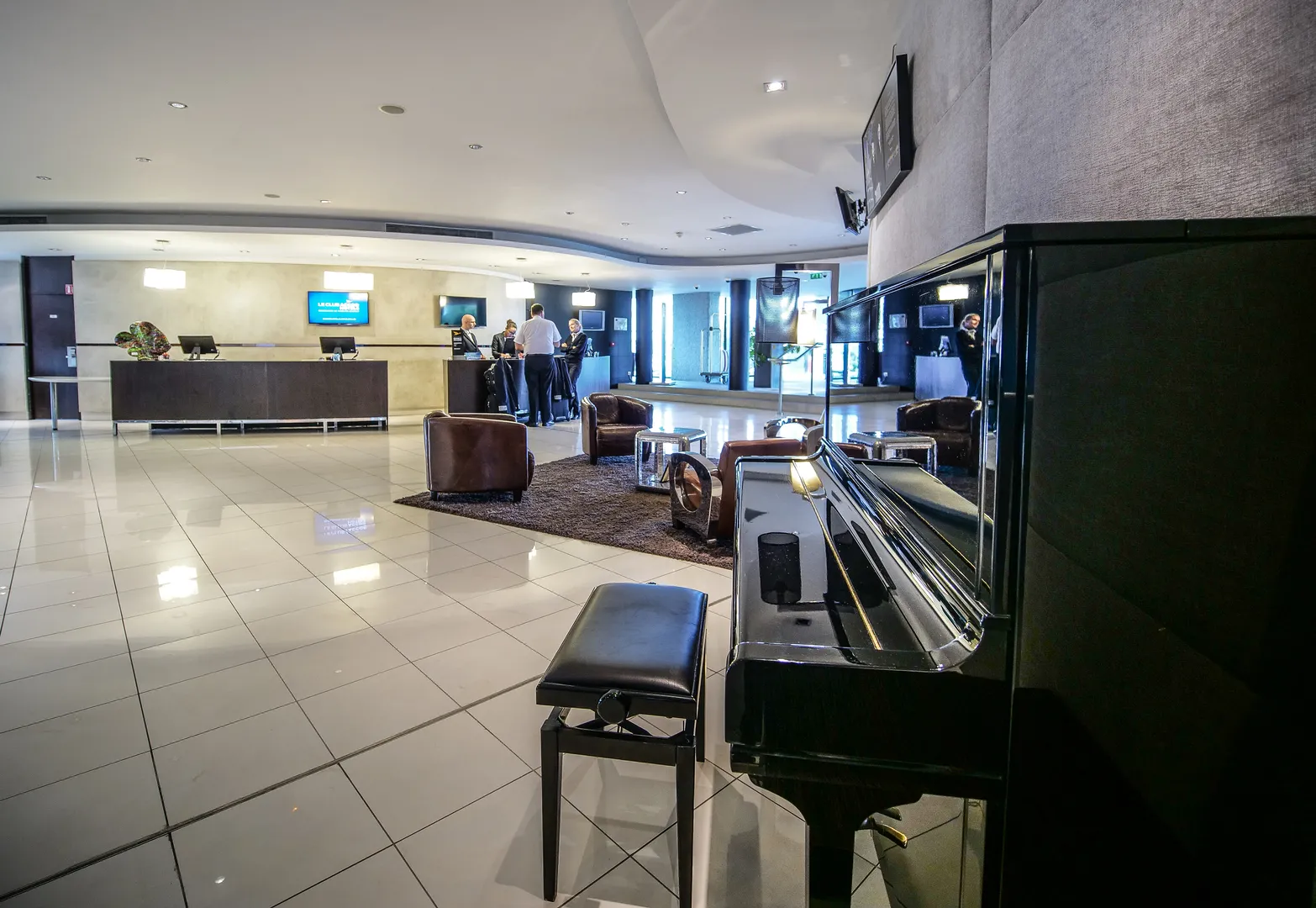 Modern lobby of Pullman Bordeaux Lac hotel featuring a black grand piano, contemporary furniture, reception desk and guests in the background