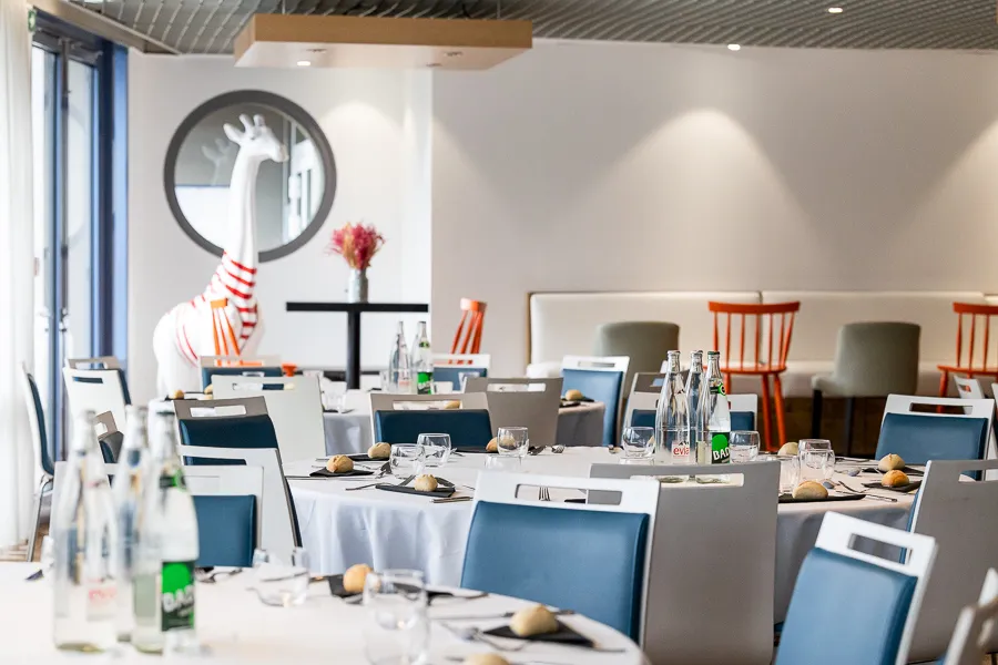 Elegant restaurant dining room with set tables, blue and orange chairs, modern décor featuring a white giraffe sculpture, at Bistrot de Mériadeck in Bordeaux